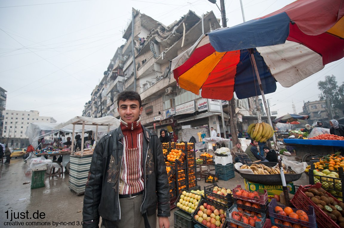 Aleppo – Boy at a fruit market beneath a shelled building